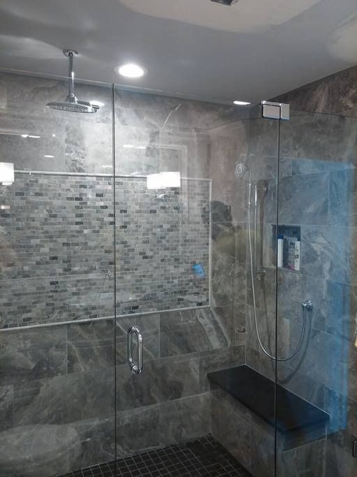 Modern gray tiled shower with glass doors, built-in bench, and rain showerhead.