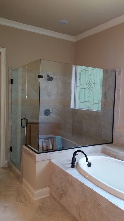 A modern bathroom with a glass shower enclosure and a built-in tub. Beige tile, light walls, dark fixtures.