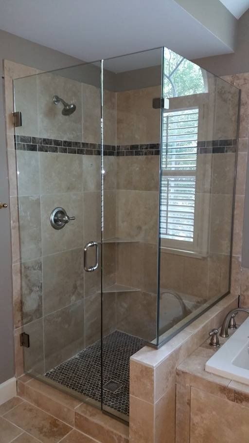 Glass-enclosed shower with beige tile walls, a dark stone floor, and a small window visible.