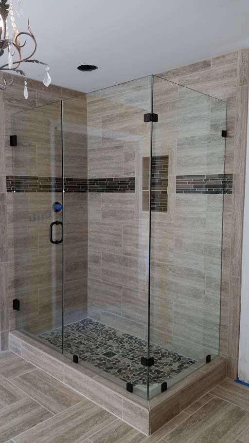 Glass shower enclosure with stone floor and tiled walls.