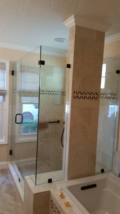 Glass shower enclosure with black hardware, next to a bathtub and tiled column.