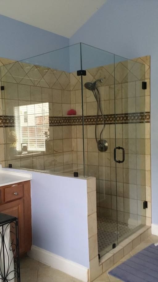 Corner glass shower with tan tiled walls, black hardware, and a shower head.