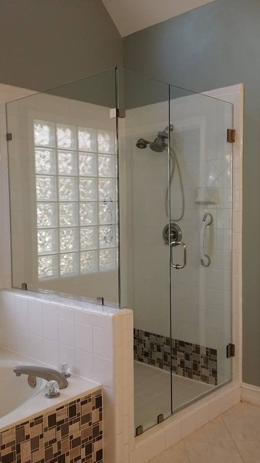 Glass shower enclosure with glass block window and tiled floor.