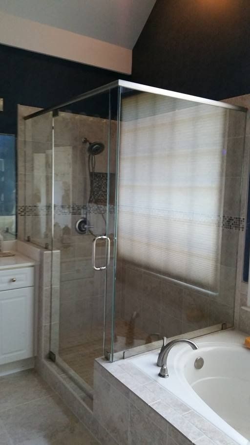 Shower stall with glass door next to a bathtub in a bathroom with beige tiles and dark blue walls.
