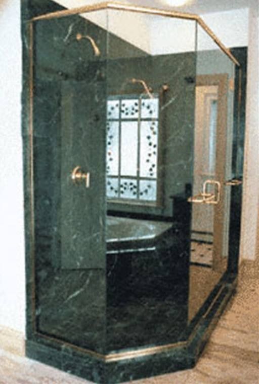 Luxurious emerald green marble shower enclosure with gold trim and fixtures, next to a window.