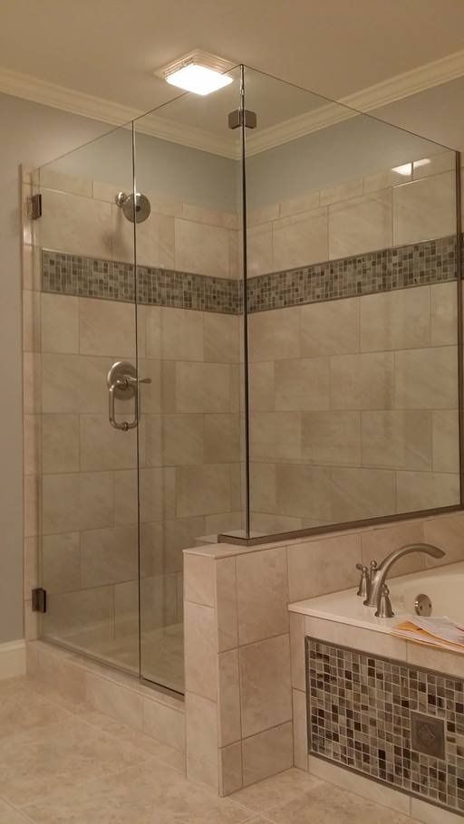 Glass shower enclosure with beige tiled walls, contrasting dark mosaic stripe. Tub in foreground.