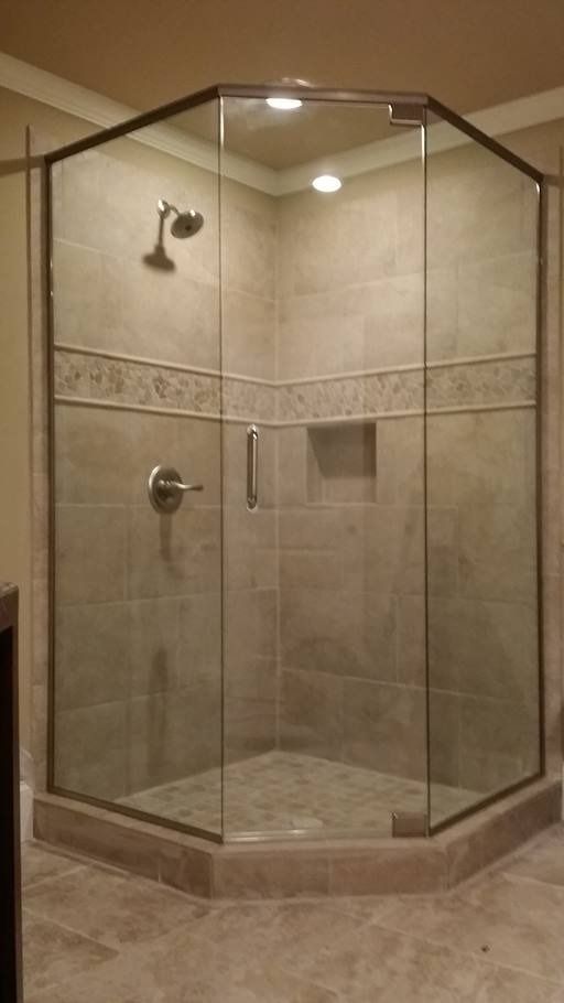 A glass-enclosed shower with brown tile walls and a stone floor; chrome shower fixtures.