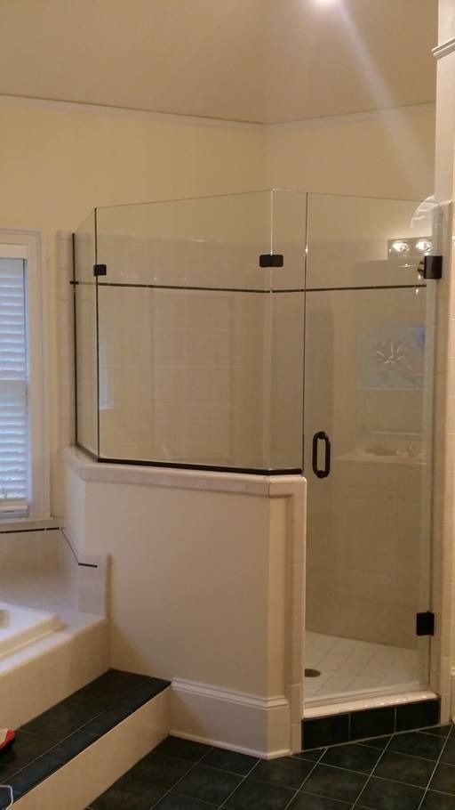 Glass shower enclosure with black hardware, on white walls, and dark green tile floor.