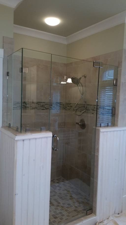 Glass shower enclosure with beige tiled walls, white wainscoting, and a rain showerhead.