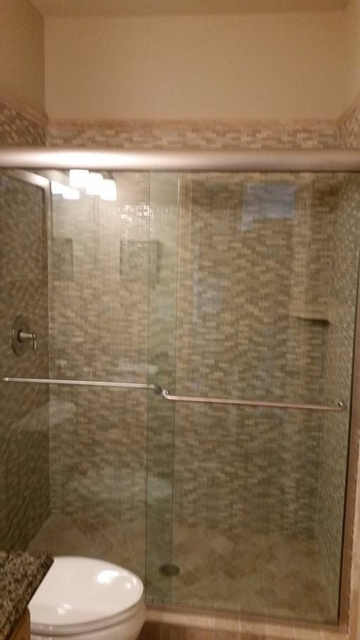 Shower stall with sliding glass doors, textured beige tile, and a toilet.