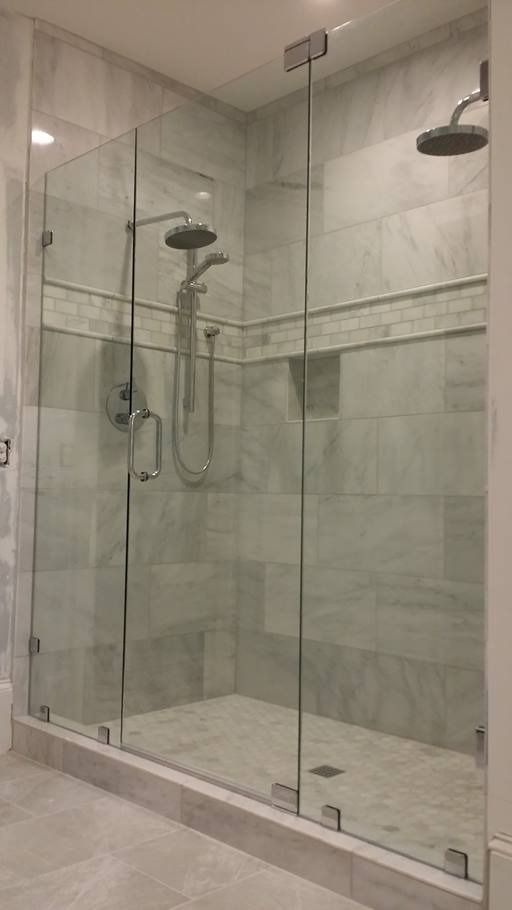 Glass shower enclosure with gray tile walls and two showerheads.