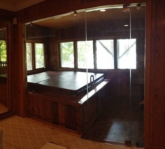 Indoor hot tub enclosure with glass doors and wood paneling. Windows offer a view.