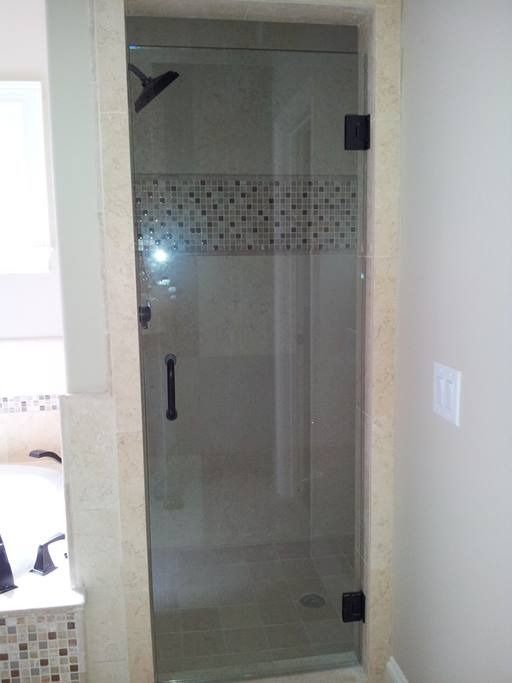 Glass shower door with black hardware, beige tiled frame, tiled wall accent.
