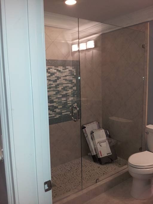 Glass shower enclosure with mosaic tile accent, pebble floor, and toilet.