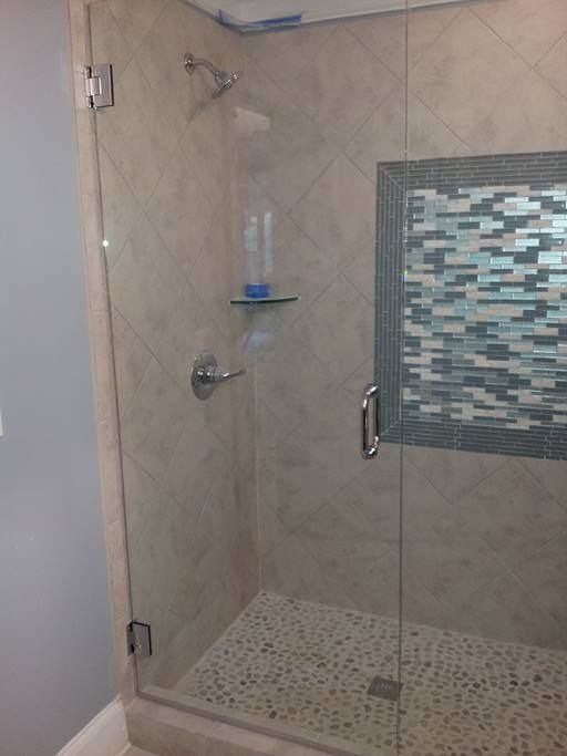 Glass-enclosed shower with beige tile walls and pebble floor. Blue and gray mosaic tile accent.