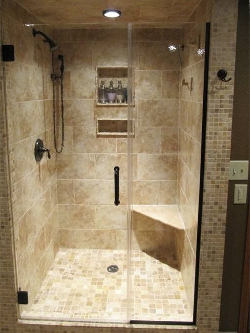 Shower with tan tiles, glass doors, built-in seat, and recessed shelves for toiletries.