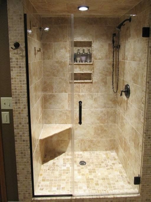 Shower with glass door, beige tile, corner seat, recessed shelves.