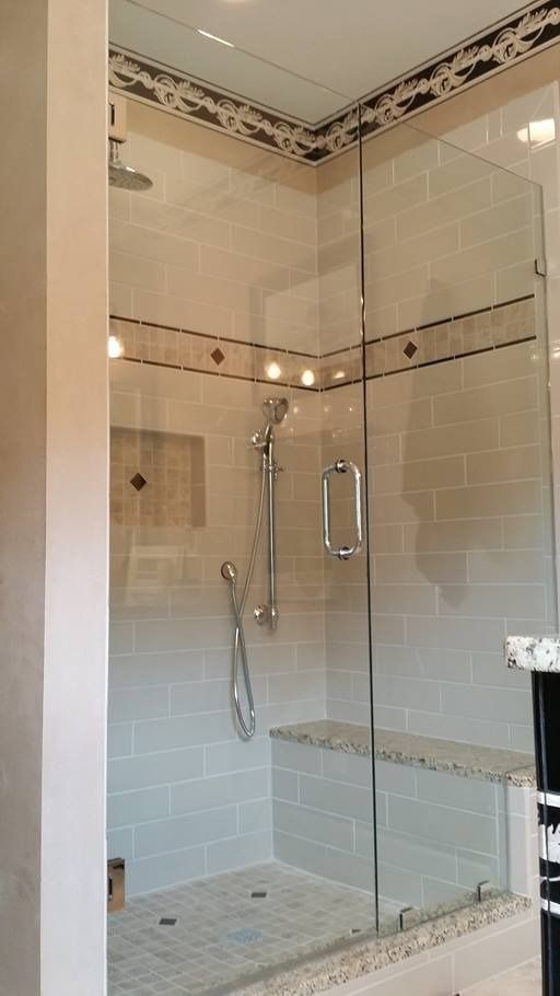 Glass-walled shower with tiled walls and bench. Silver shower fixtures and a decorative tile band.