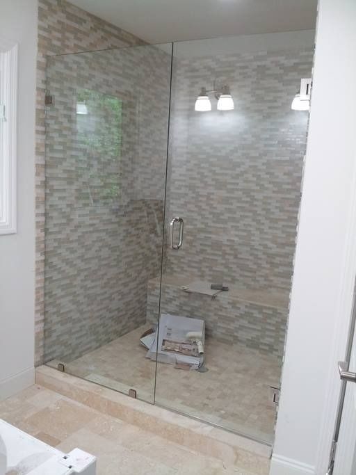 Glass shower enclosure with mosaic tile walls and a light-colored stone floor.