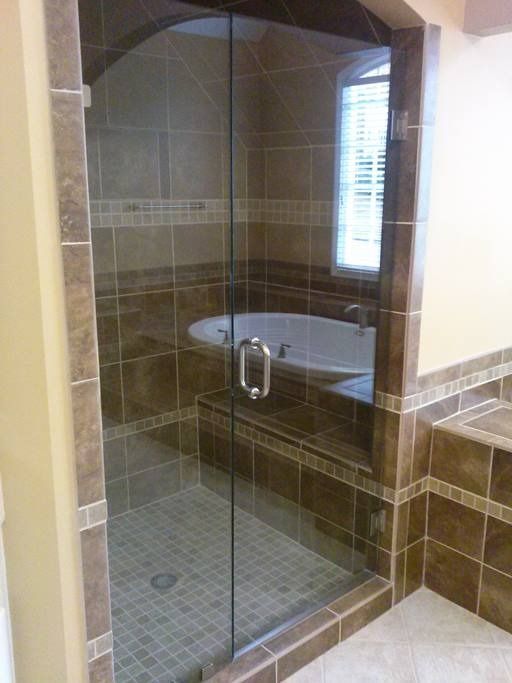 Glass shower enclosure with brown tile walls and a built-in bathtub.