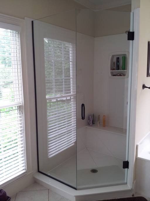 Glass shower enclosure in a corner of a bathroom with blinds and toiletries.