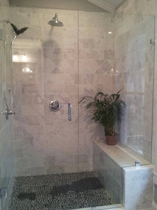A modern shower with glass walls and pebble floor. It features a built-in bench with a potted plant.
