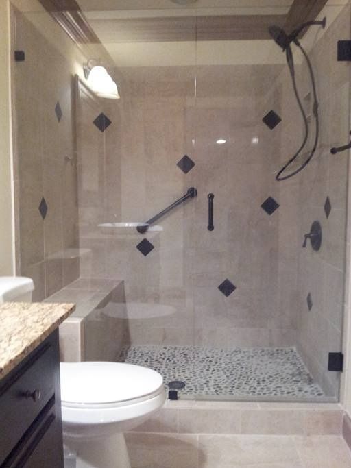 Shower with clear glass doors, light beige tile, black accents, and a pebble floor.