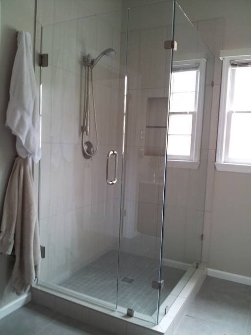Glass shower enclosure with chrome fixtures and white robe hanging outside.