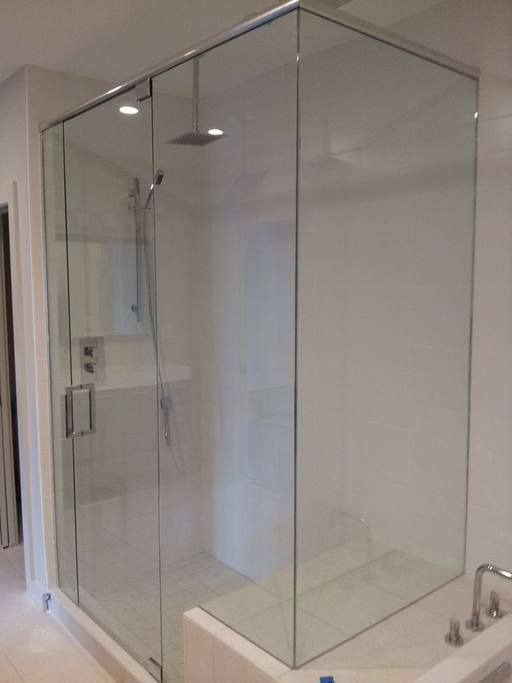 Glass shower enclosure with sliding door, showerhead, and fixtures in a white bathroom.