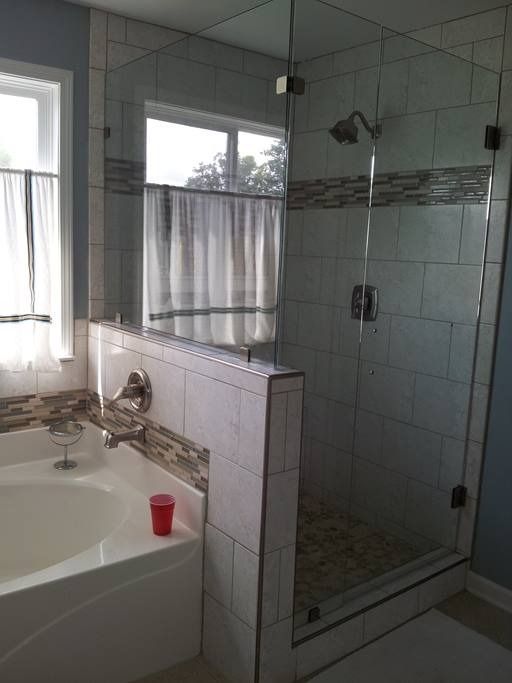 Bathroom with glass shower, white tile, and a bathtub with a window.