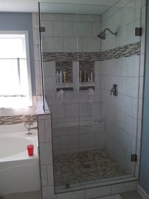 Glass shower enclosure with tiled walls, built-in shelving, and pebbled floor.