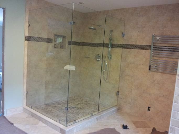 Glass shower enclosure with beige tiled walls, showerhead, and towel rack.