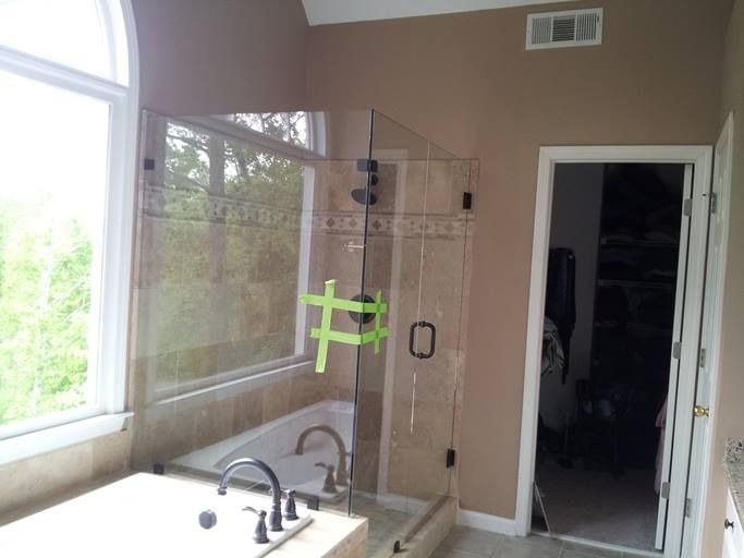 Bathroom with glass shower, bathtub near window, tan walls.