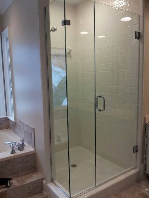 Glass shower enclosure with door, mounted on a stone base, adjacent to a tub.