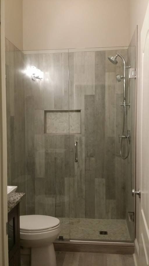 Gray tiled shower with glass door and rain showerhead, next to a toilet.