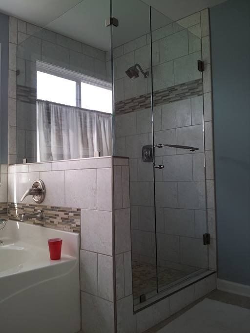 A bathroom with a white bathtub and glass shower door. Light blue walls and tiled surfaces.