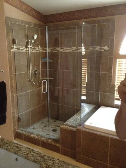 Shower with glass doors and brown tile, next to a bathtub.