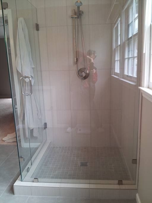 Glass-enclosed shower with a gray tiled floor, shower head, and a white robe hanging on the door.