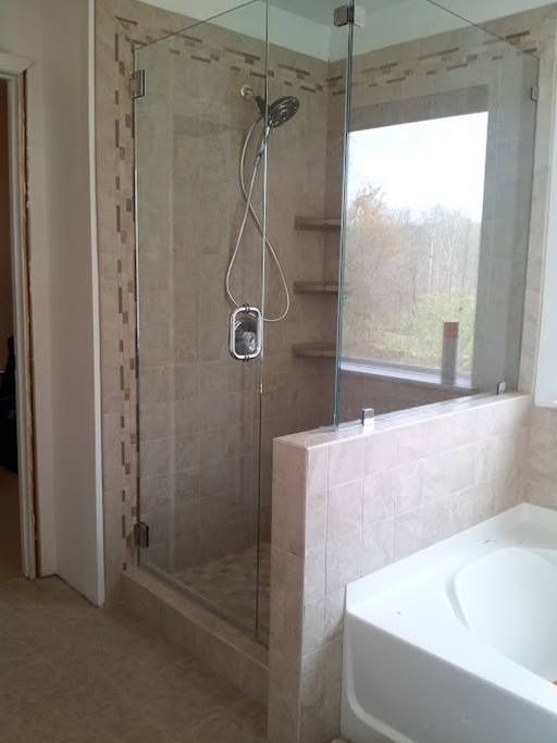 Bathroom with beige tiled shower stall, glass door, and a built-in shelf.