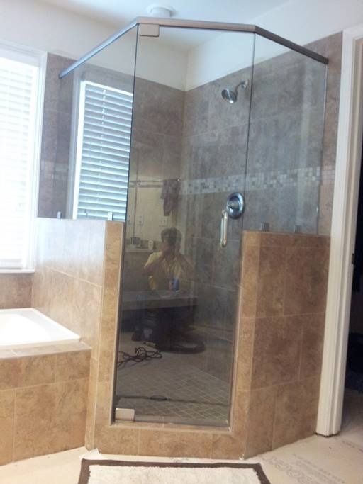 A walk-in shower with glass doors and tile walls. A reflection of a person is visible in the glass.