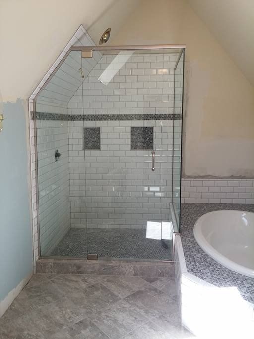 A frameless glass shower enclosure in a bathroom with white subway tile and a slanted ceiling.