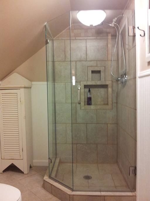 A tiled shower with a glass door, built into an angled attic wall, with a cabinet on the left.