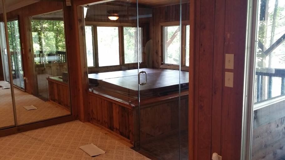 Indoor hot tub enclosed by glass and wood, surrounded by wood paneling and mirrors.