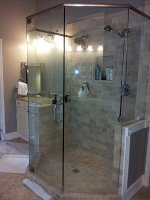 A glass-walled, tiled shower in a bathroom.  Includes a shower head, shampoo niche, and a door.