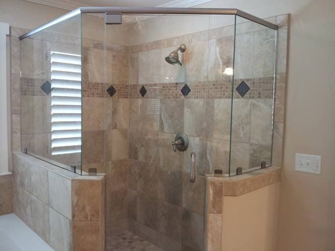 Glass shower enclosure with beige tiled walls.