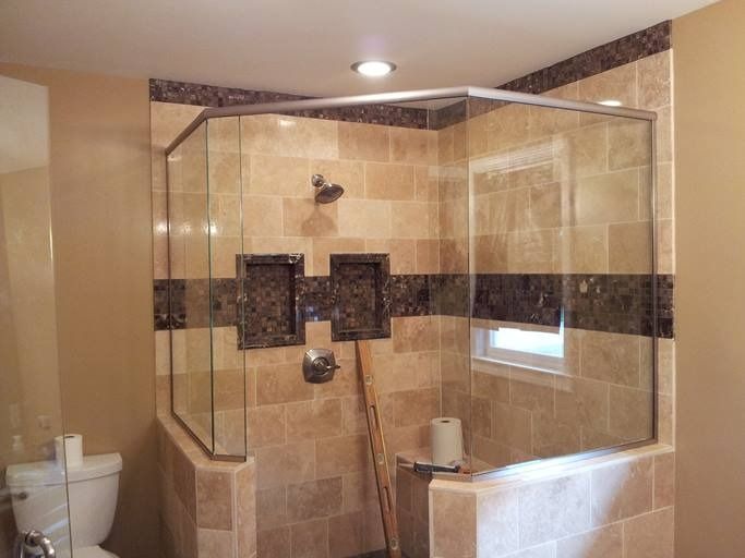 A large, tiled shower with glass doors and a dark marble accent band; a toilet is visible to the left.