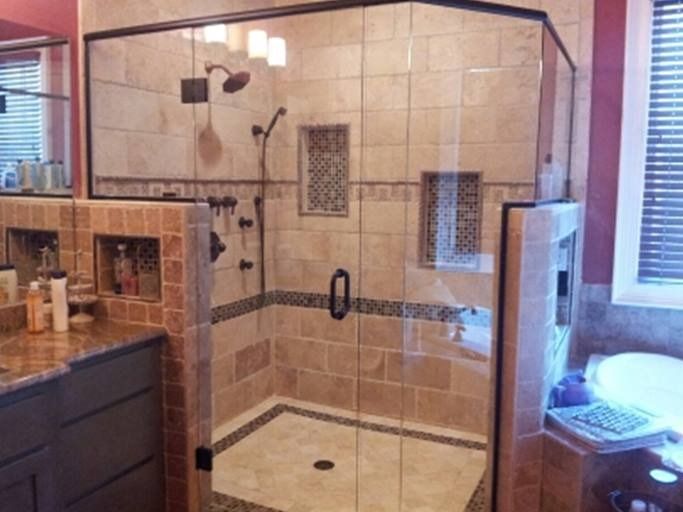 Bathroom with a tiled shower stall and glass door, beige and brown tones, built-in shelving.