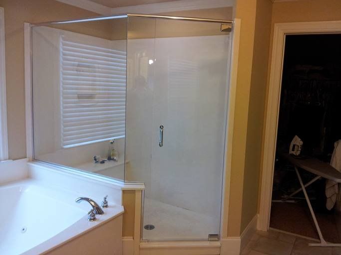 Glass shower enclosure next to a jacuzzi tub, with a door and handle; beige walls and an open closet.