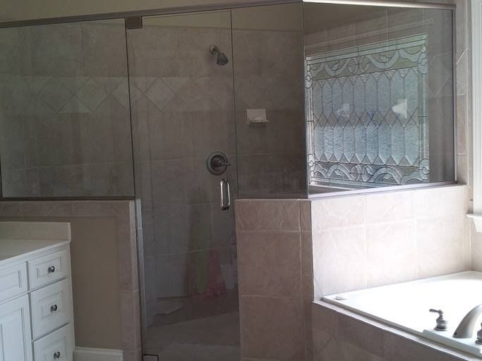 Glass-enclosed shower with tiled walls and a small tub. Includes a frosted window and white vanity.