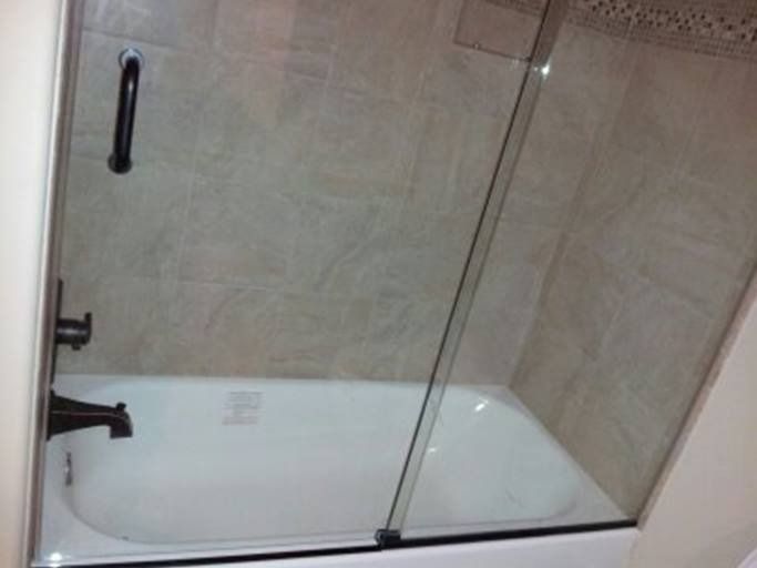 Bathtub with glass shower door, dark fixtures, and beige tile walls.